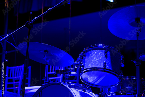Blue illuminated jazz drum set on concert stage with copy space, Jazz drum set illuminated with blue stage lights during concert preparation. Rich monochromatic tones and generous copy space 