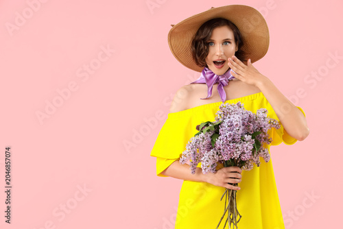 Surprised young woman with bouquet of blooming lilac flowers on pink background