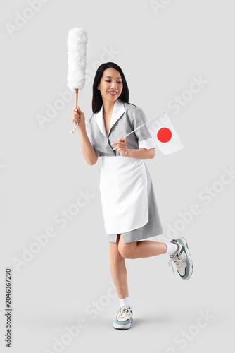 Young Asian chambermaid with pp-duster and flag of Japan on light background