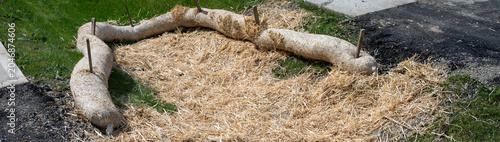 Straw wattle in stormwater drainage ditch  and straw scattered over grass  to filter out construction debris  concrete sidewalk and asphalt road 