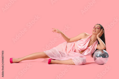 Stylish young woman with disco ball on pink background