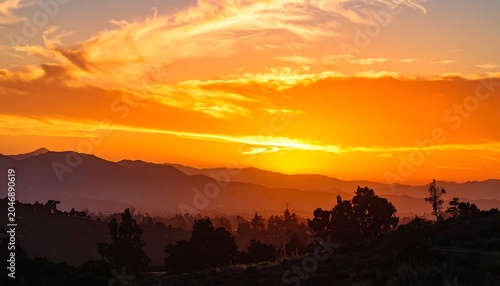 A vibrant sunset paints the sky with fiery hues. Silhouetted mountains and trees create a serene and majestic landscape