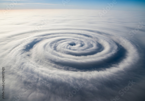 Aerial view of a massive spiral cloud formation swirling above the ocean under a blue sky.