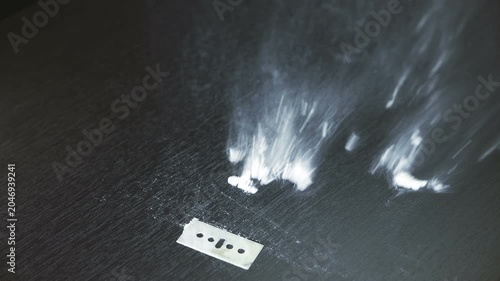A line of cocaine or methamphetamine cut on a table next to a razor blade being blown away in slow motion. Addition treatment, quitting drugs.