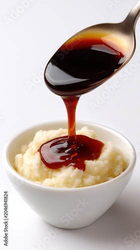Soy sauce being poured from a silver spoon onto a bowl of white rice