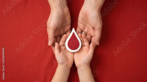 Hands holding a red blood drop on a red background symbolizing donation