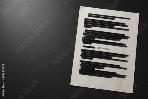 Redacted confidential document on dark surface. Space for text.