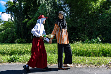 A hijab-wearing mother takes her daughter, who is wearing an elementary school uniform, to school. Asian Indonesian woman. Education Day concept. Back to school. Mother's Day concept.