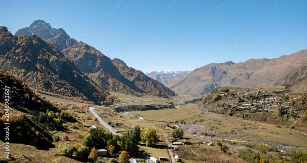 Fototapeta premium Scenic view of mountains and valley with small village during clear day in the Caucasus region of Georgia