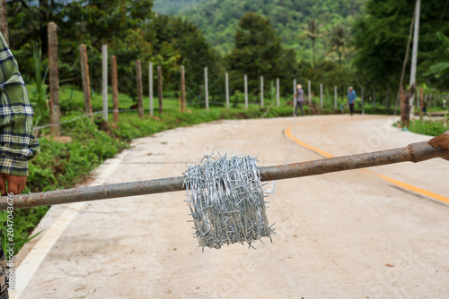 Konstfotografi Focused rural worker carry heavy barbed wire roll on wooden pole across concrete