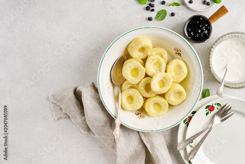 Top view of homemade sweet cottage cheese lazy pierogi or curd dumplings with sour cream and blueberry jam on white concrete background flat lay