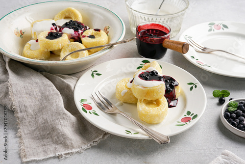 Side view of homemade sweet cottage cheese lazy pierogi or curd dumplings served with sour cream and blueberry jam on white plate, traditional breakfast food photography