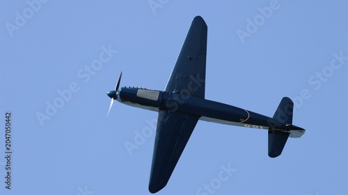 View of a vintage propeller plane performing a flight maneuver against a clear blue sky during an airshow in La Ferte-Alais, Ile-de-France, France.
