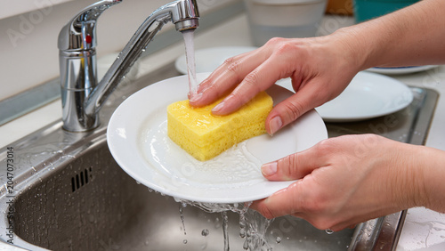 Bilde på lerret Washing plates by hand in a kitchen sink