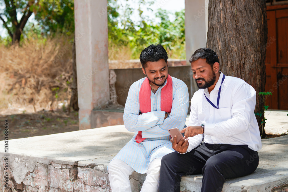 Obraz premium Indian banker or agronomist showing some detail in smartphone to farmer