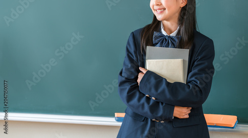 Foto Female elementary, middle, and high school students in school uniforms, holding textbooks, standing in front of the classroom blackboard