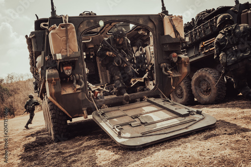 Valokuva Action shot of soldiers in full combat gear running out from the open back ramp of a military transport vehicle during a fast-paced assault simulation in a dusty field