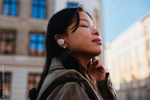 Woman listening with earbuds while standing in city