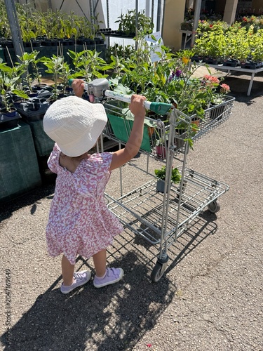 Obraz na płótnie Enfant avec chapeau poussant un chariot de plantes dans un jardin en plein air