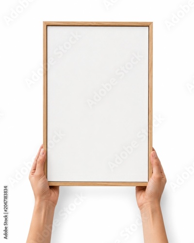 Pair of hands holding a blank white vertical canvas mockup with a slim natural wood frame canvas held from the bottom edge with fingers mostly hidden behind the frame