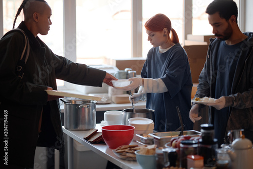 Obraz na płótnie Young adult volunteers serving meals to people in need at humanitarian aid center, supporting community relief and food assistance