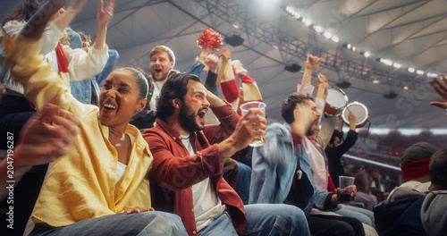 Black Woman in Yellow and a White Man With Red Face Paint Join Diverse Soccer Football Supporters in Stadium, Yelling, Lifting Hands, Drinking Beverage, Beating Drums. Fun Authentic Style
