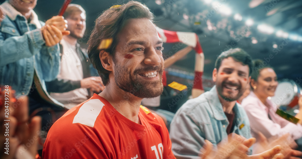 Naklejka premium Close Portrait of White Male Soccer Football Supporter With Red and White Face Paint, Smiling in Packed Championship Stadium as Diverse Fans Wave Flags and Cheer During Intense Cup Tournament Match.
