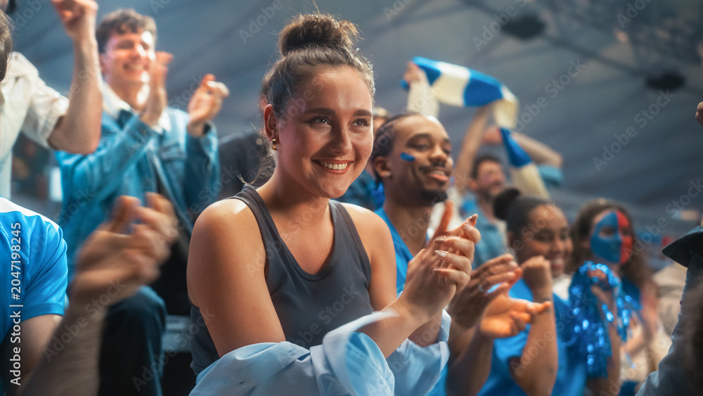Naklejka premium Portrait of a Smiling White Female Spectator Applauding During a Soccer Football Championship Match in a Stadium, Excited Diverse Crowd of Happy Fans Cheering and Celebrating a Victory at a Game.