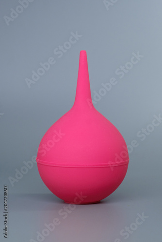Pink rubber medical syringe bulb on a grey background. Disposable rubber enema bulb syringe for medical and newborn hygiene procedures.