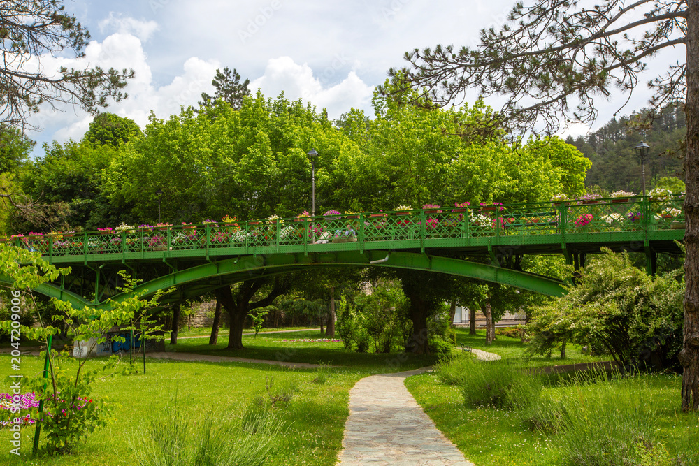 Fototapeta premium Beautiful arched pedestrian bridge with colorful flowers in a green park of Jajce, Bosnia and Herzegovina
