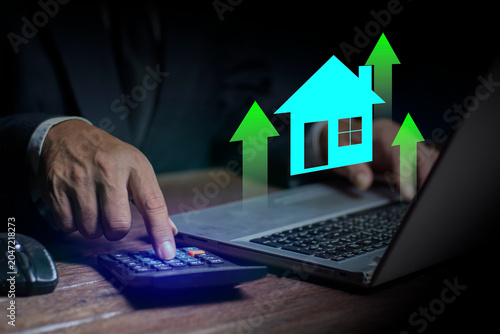 Real estate concept business, businessman with house icons with growth arrows above a laptop, Buy and sell houses and real estate online on a virtual screen.