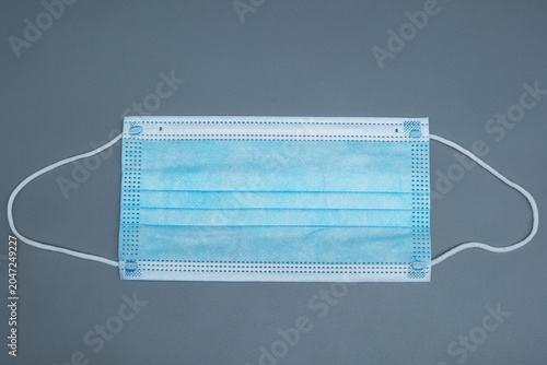 Disposable blue medical face mask on a grey background. Protective 3-ply surgical mask with ear loops on a neutral grey surface, top view.