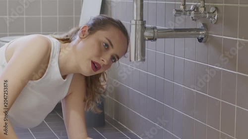 Worried young woman looking at leaking pipe under bathroom sink home emergency