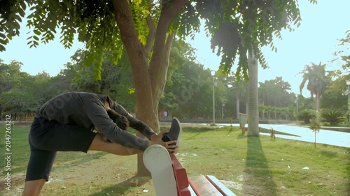 Indian sportsman doing stretching exercises in the morning - healthy lifestyle. Medium shot of an athlete in a T-shirt and Shorts with Bluetooth headphones listening to music while exercising
