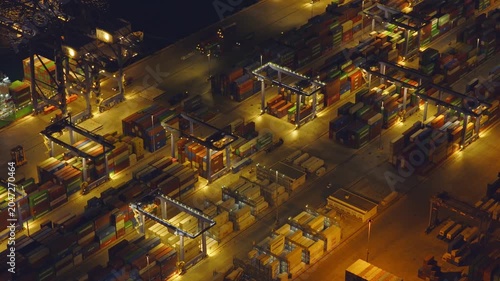 High-angle view of a bustling commercial port at night, with illuminated gantry cranes moving shipping containers in a global logistics and transportation hub, showcasing international trade