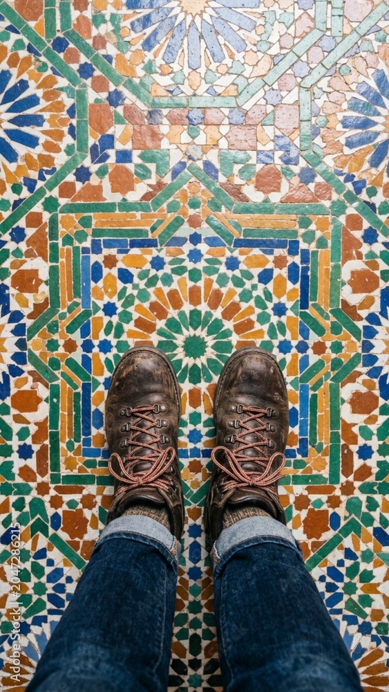 Fototapeta premium Brown leather hiking boots standing on Moroccan zellij mosaic tile floor with geometric star patterns