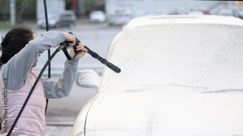 This video captures the moment a woman apply washing foam to wash her car at a self-service station. The rhythmic motion of the sponge and spray brings life to the joy of car care on a sunny day.