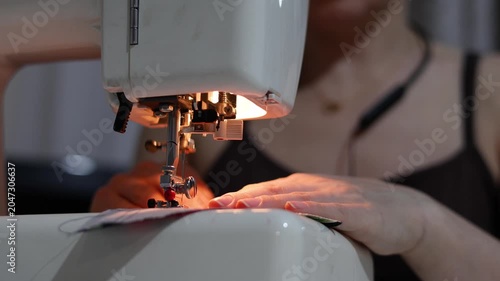 Close-up footage shows hands working diligently with a sewing machine, stitching blue fabric. The careful guidance and smooth stitching reflect skill and focus on creating flawless seams.