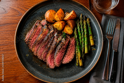 Overhead view of sliced beef steak with roasted potatoes and asparagus