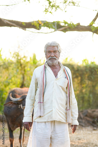 Photography An elderly farmer stands in a rural farmyard with buffaloes in the background
