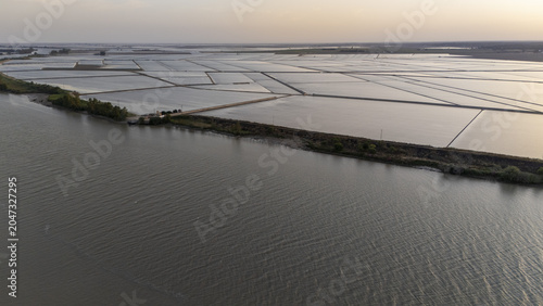 Aerial view of the Guadalquivir river flowing past flooded rice fields under a soft hazy sky in Coria del Rio, Andalusia, Spain.