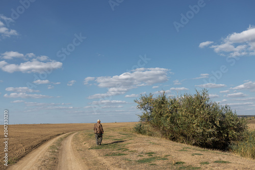 Mature man hunter with gun while walking on field.