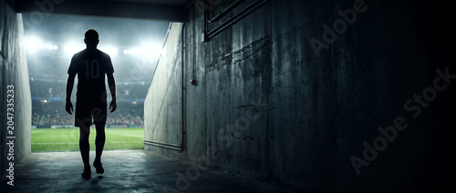Lone Football Player Walks Out of Dark Tunnel Towards Bright Stadium Field