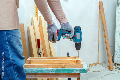 Фотография Woman carpenter using cordless drill to make hole in wooden plank