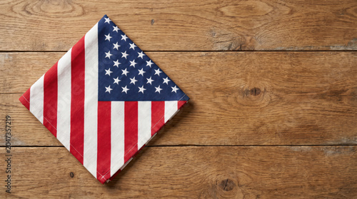 Folded American flag napkin on natural wooden table with generous copy space, patriotic dining background for USA Independence Day celebrations, summer gatherings and holiday events