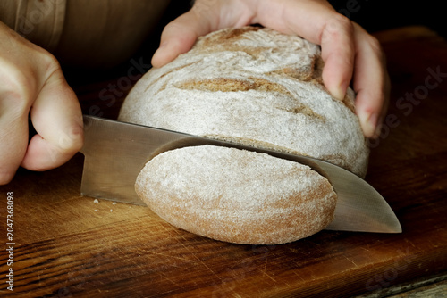Hands slicing loaf of brown bread on cutting board