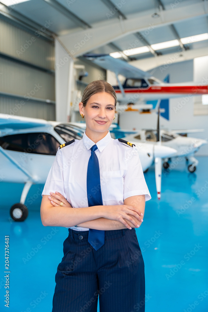 Fototapeta premium Confident female pilot standing in aircraft hangar