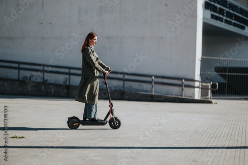 Fotografie Young woman rides an electric scooter across a concrete urban plaza