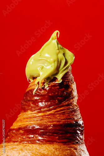 Melting green pistachio cream on flaky golden croissant over red