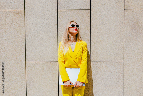 Happy freelancer wearing yellow suit holding laptop outside